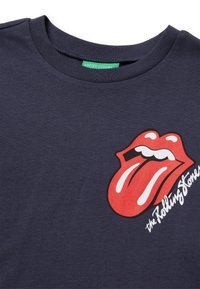 Námornícká modrá bavlněná tričko s velkým logem červených rtů a jazyka potištěným na přední straně, s textem "the Rolling Stones" v bílé barvě.