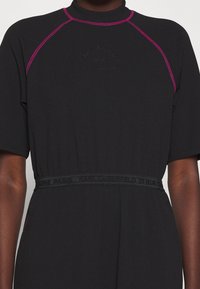 Robe noire à manches courtes avec des accents de coutures roses, un col montant et une taille élastique présentant une discrète marque en relief "Karl Lagerfeld Paris".