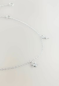 Delicate silver chain bracelet with a small star-shaped charm featuring a central clear gemstone on a light background.