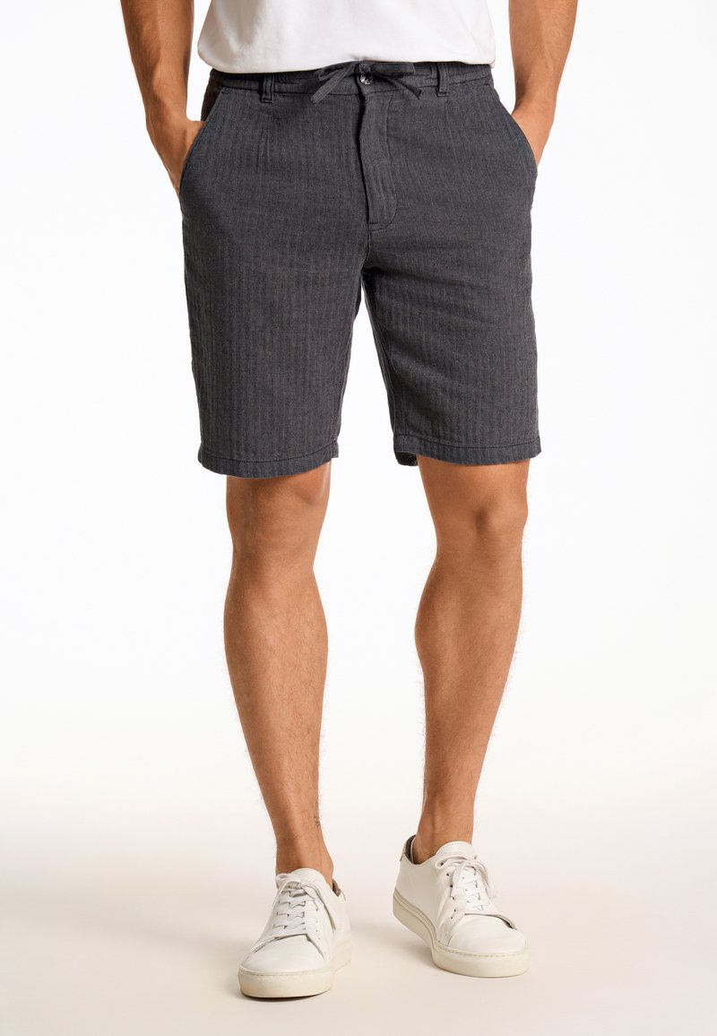 Shorts rayés gris en tissu texturé, dotés d'une fermeture à bouton et zip, de passants de ceinture et de poches latérales, associés à des baskets blanches.