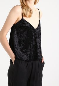 Camisola in velluto nero con spalline sottili, scollatura a V e vestibilità ampia. Presenta una superficie morbida e testurizzata e cade appena sotto la vita.