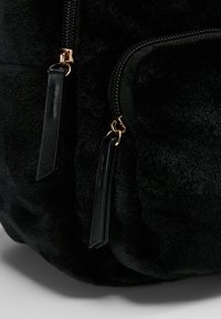 Gros plan sur un sac en tissu pelucheux noir avec deux curseurs de fermeture éclair en cuir noir et une fermeture éclair en métal doré.