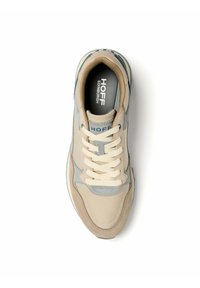 Zapatilla deportiva en color beige y gris con parte superior de cuero y tela suave, puntera redonda, cordones crema y logo de la marca en la lengüeta y en la plantilla.