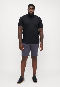 Tricou polo negru cu guler, combinat cu pantaloni scurți gri. Modelul poartă adidași negri. Textură de țesătură netedă, design simplu, fără modele.