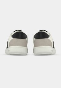 Baskets blanches et grises avec une texture lisse, des accents noirs et un design à tige basse. Panneaux en daim discrets au talon et sur les côtés.