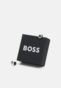 Ciorchini metalici cu un detaliu circular albastru marin, așezați lângă o cutie neagră cu text alb "BOSS" pe față.