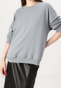 Ljusgrå sweatshirt i mjukt material med avslappnad passform, ribbade manschetter och rundad halsringning, kombinerad med en svart läderkjol.