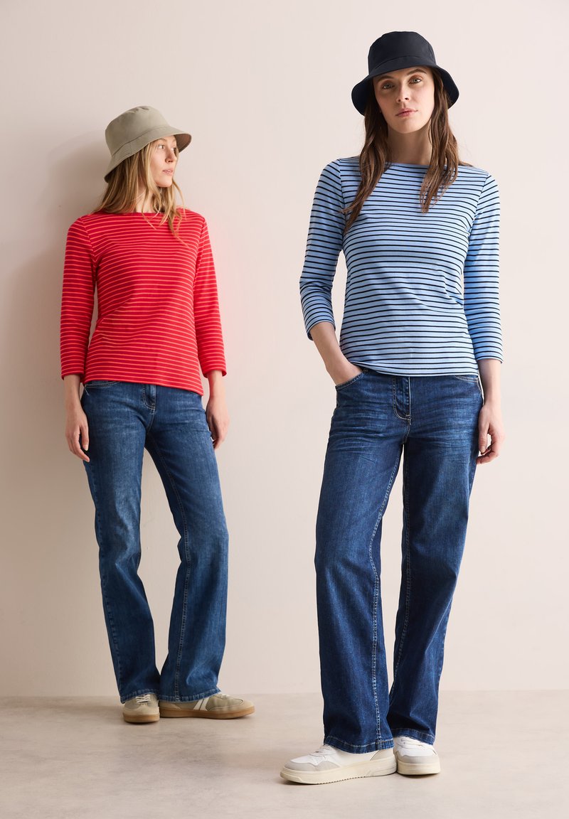 Rood gestreepte langemouwen shirt met een ronde halslijn en een blauwe gestreepte variant. Beide in combinatie met blauwe jeans en informele schoeisel, met emmerhoeden.