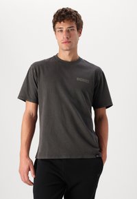 Camiseta gris de manga corta con cuello redondo, que presenta un pequeño logo en el pecho. Fabricada en un tejido suave con una textura lisa.