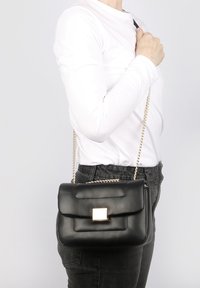 Borsa a tracolla in ecopelle nera con chiusura dorata, tracolla a catena, texture trapuntata, forma rettangolare e design elegante e minimalista.