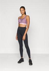 Μωβ αθλητικό σουτιέν με ανοιχτό ροζ λωρίδα, σετ με μαύρο κολάν ψηλόμεσο. Απλός, εφαρμοστός σχεδιασμός χωρίς ορατά μοτίβα. Μαύρα παπούτσια.