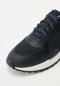 Donker marineblauwe sneaker met een combinatie van textuurmesh en glad leer, ronde neus, platte veters en een witte, gegroefde zool.