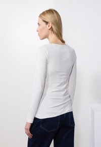 Weißes Langarmoberteil mit Rundhalsausschnitt, figurnaher Passform und glatter Textur, kombiniert mit dunkelblauen High-Waist-Jeans.