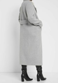 Szary, długi wełniany płaszcz z dopasowanym kołnierzem, bocznymi kieszeniami i paskiem w talii. Noszony z błyszczącymi czarnymi kozakami do kolan.