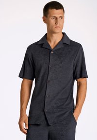 Camicia a maniche corte, con bottoni, di colore grigio scuro, realizzata in tessuto morbido con una superficie testurizzata e colletto classico. Presenta bottoni marroni.