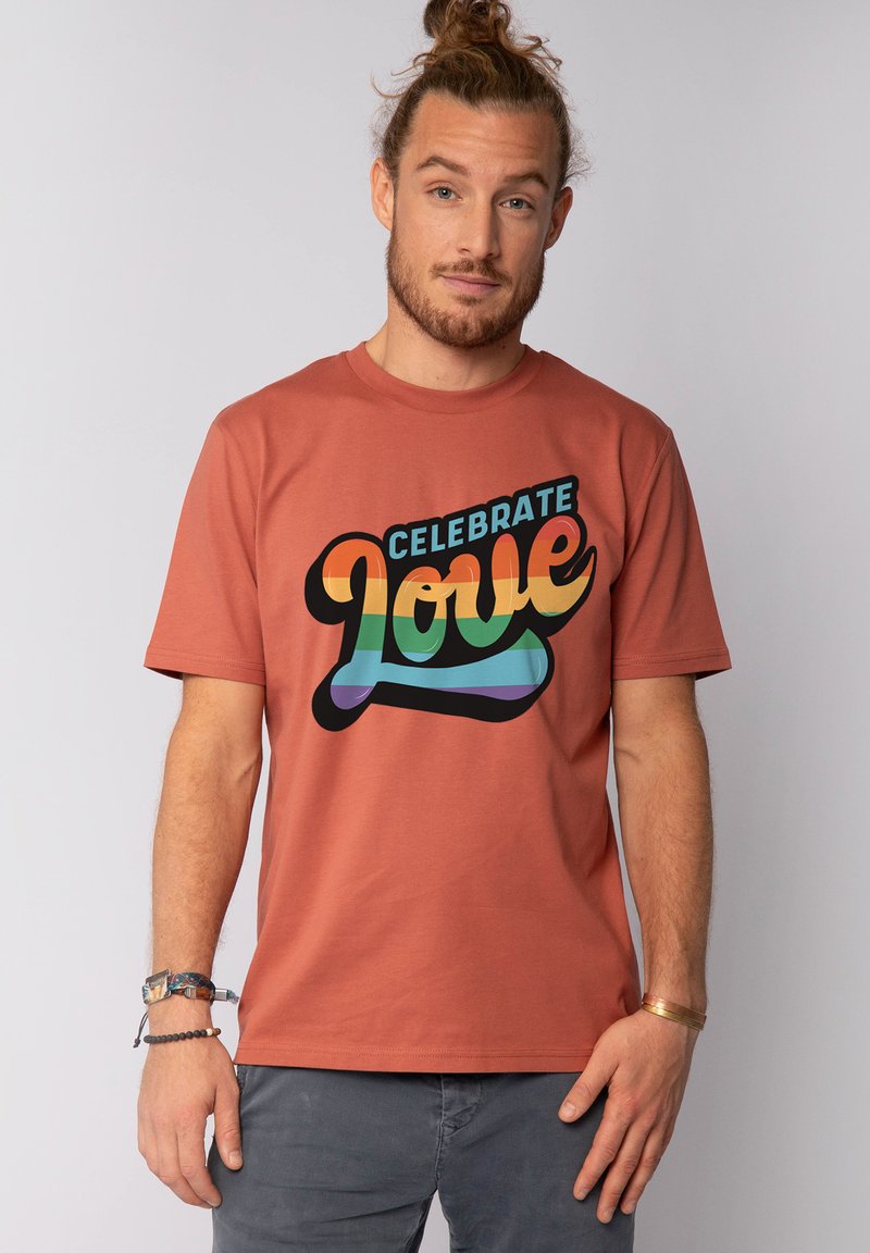 T-shirt à manches courtes de couleur rouille avec un graphique "CÉLÉBREZ L'AMOUR" en couleurs vives et dans une police arrondie. Tissu en coton doux, coupe décontractée.