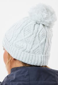 Lys blå strikket hat med kabelmønster, en fluffy pom-pom på toppen og subtile glitrende detaljer integreret i garnet.