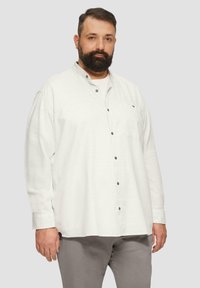 Lichtgekleurde langslibshirt met een kraag, voorzien van donkere knopen en een borstzak, gecombineerd met grijze broek. Gladde textuur.