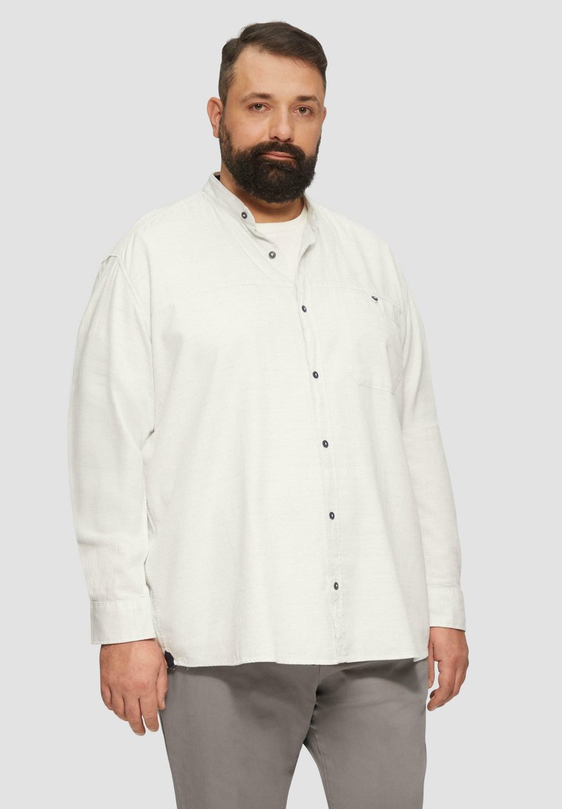 Lichtgekleurde langslibshirt met een kraag, voorzien van donkere knopen en een borstzak, gecombineerd met grijze broek. Gladde textuur.