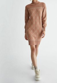 Robe pull tricotée en rose poussiéreux avec motif logo ton sur ton, col montant côtelé et manches bouffantes. Stylée avec des baskets montantes blanches.