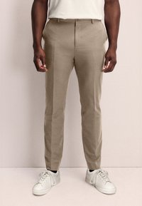 Pantalones beige de corte ajustado, hechos de una tela ligera, con bolsillos laterales y un diseño de frente plano. Combinados con zapatillas blancas.