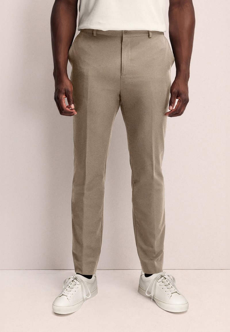 Beige broek met een slim fit, gemaakt van lichtgewicht stof, met zijzakken en een platte voorkant. Gecombineerd met witte sneakers.