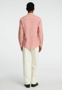 Camisa de manga larga roja con textura, con sisa en la espalda, dobladillo curvado y puños de botón, combinada con pantalones amplios blancos y zapatos negros.