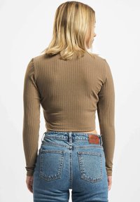 Pruun ribaga pikki varrukatega crop-top, mis on sobitatud kõrge vöökohaga siniste teksadega, mille taga on nahast brändipatch.