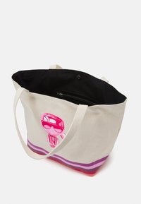 Canvas tote bag med rosa tecknad karaktär som bär solglasögon och randig botten i lila och rött, öppen topp som visar en svart innerväst.