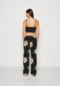 Svart kort topp i kombination med lösa, svarta byxor med blommönster som har stora beige blommor och gröna blad. Vita sneakers synliga.