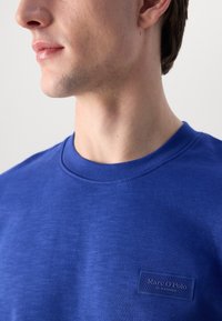T-shirt in cotone blu con scollatura rotonda, caratterizzato da una finitura testurizzata e da un piccolo logo ricamato sul petto. Design minimalista.