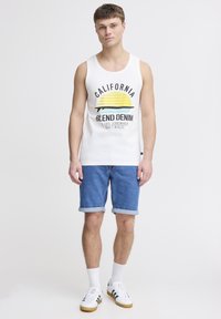 Top fără mâneci alb, cu un design grafic galben și verde, având inscripțiile "CALIFORNIA" și "BLEND DENIM", asortat cu șorturi din denim.