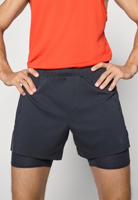Męskie szorty sportowe z czarnego materiału, wyposażone w elastyczny pas, dopasowaną wewnętrzną podszewkę i boczne panele wentylacyjne.