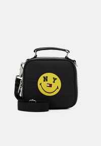 Borsa quadrata in nylon nera con un patch a forma di faccina sorridente gialla che presenta "NY" e un piccolo logo della bandiera. Include una maniglia corta e una tracolla removibile.
