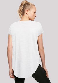 White short-sleeve shirt with a rounded hem, made of lightweight fabric. Back view shows relaxed fit and subtle texture. Worn with black leggings.