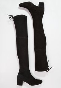 Botas negras por encima de la rodilla, hechas de suave ante, con un tacón cuadrado; presentan un detalle de lazo en la parte superior y un diseño de punta redondeada.