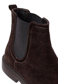 Donkerbruine suède Chelsea-boot met elastische zijpaneel en een aantrekloop aan een lage gestapelde hak.