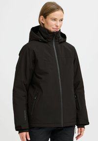 Svart vanntett jakke med hette, glidelås foran, to sidelommer, justerbare funksjoner og teksturert stoff, designet for utendørs bruk.