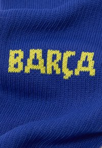 Sinine kudum, millel on särav kollane sõna "BARÇA". Kujundusel on tekstureeritud pind, millel on üle kogu pinna soonikmuster.