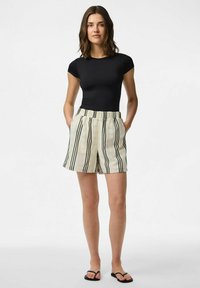 Top nero aderente abbinato a pantaloni beige con strisce verticali nere e un tessuto texture; i pantaloni hanno tasche laterali e una vita elastica.