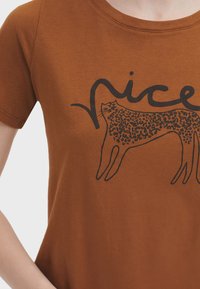Brun bomuld t-shirt med et sort leopardgrafik og ordet "nice" ovenfor. Kortærmet og med rund halsudskæring. Glat tekstur.