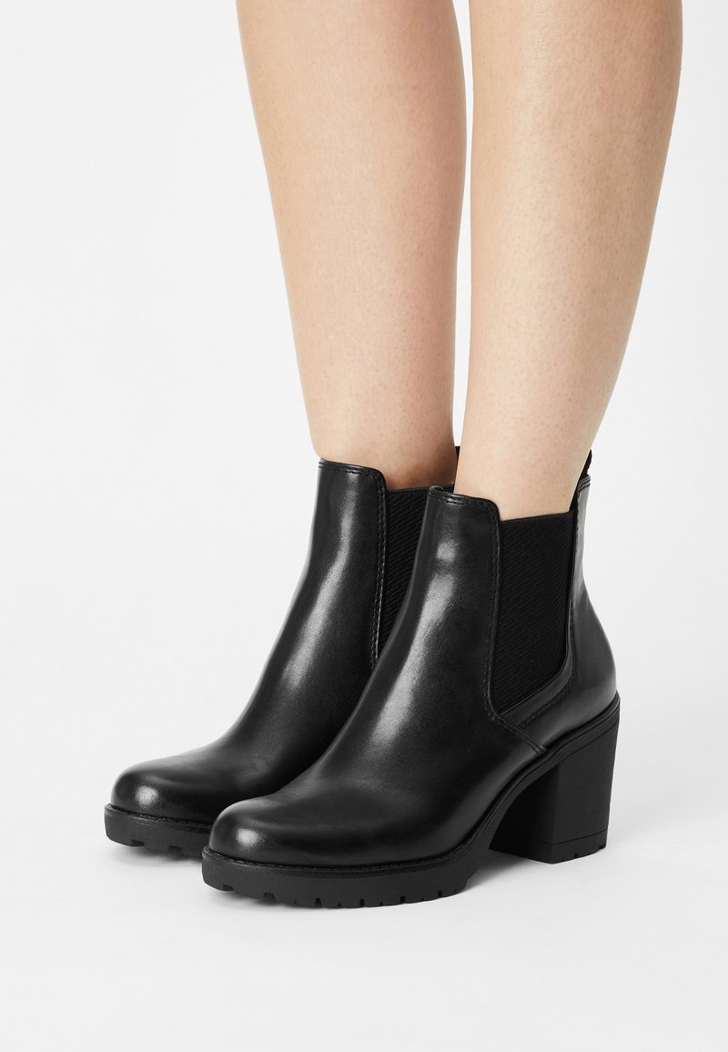 Black leather ankle boots with a chunky heel, elastic side panels, and a smooth surface, featuring a rounded toe and textured accents.