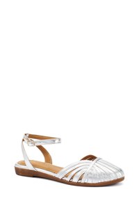Sandali piatti metallici argento con cinturino alla caviglia, design con punta aperta, cinturini frontali incrociati e soletta testurizzata. Suola piatta per il massimo comfort.