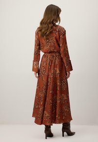 Vestido marrón con estampado floral, mangas largas, cintura ajustada y falda fluida. Presenta patrones florales oscuros y un detalle fruncido en la parte trasera.