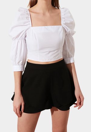 Witte cropped top met pofmouwen en vierkante halslijn, gecombineerd met zwarte hoog-getailleerde shorts met een geschulpte zoom.