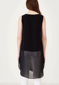 Black sleeveless tunic with a sheer lower hem, featuring a rounded neckline and flowy material, shown from the back.
