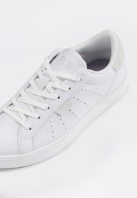 Sneaker in pelle bianca con dettagli perforati, lacci bianchi piatti e una accentuazione in suede grigia sul tallone. Logo argento sul lato.