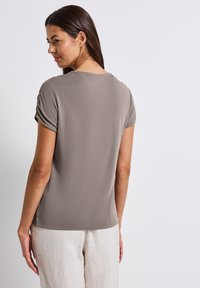 T-shirt à manches courtes, coupe décontractée en taupe avec des manches froncées et une texture lisse. Associé à un pantalon beige clair, ample.