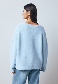 Light blue fuzzy sweater with a relaxed fit, wide neckline, and long sleeves. Paired with light denim jeans, featuring a slightly frayed hem.