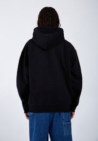 Black hoodie with a spacious design, featuring a large hood and loose-fitting sleeves, paired with blue denim pants. Smooth texture.